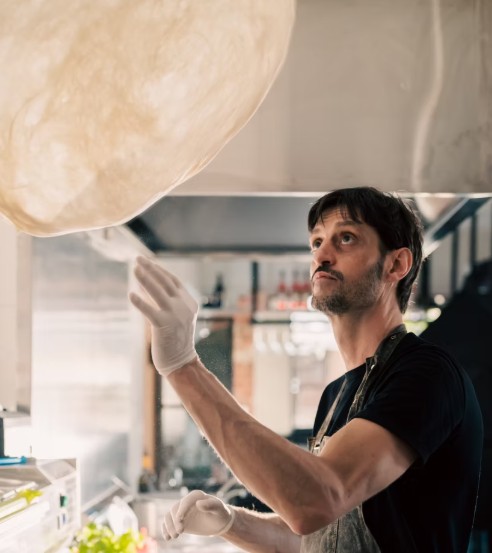 Chef stretching pizza dough by hand in the open kitchen at The Code Pizza Bar